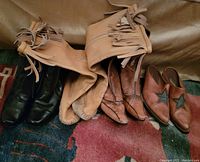 Four pairs of women's boots in various colors and styles, arranged on a carpeted floor, showing their full side profiles.
