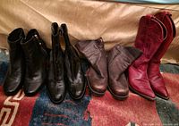 Four pairs of women's mid-height boots displayed in a row on a carpet. Includes black leather zip-up ankle boots, black pull-on boots, brown leather mid boots, and red cowboy boots.