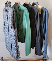 Photo of 4 women's outerwear items hanging on hangers, showing front and partial side views. Includes gray quilted vest, green jacket, dark gray jacket, blue denim jacket with shearling collar.
