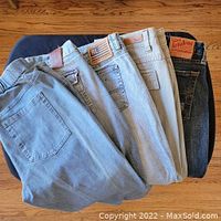 Five pairs of jeans stacked showing back pockets and labels including RL Polo and Lucky Brand