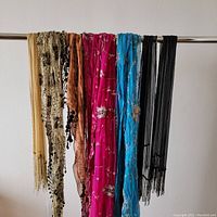 Front view of 7 hanging scarves showing various colors, beadwork, embroidery, and fringe details.