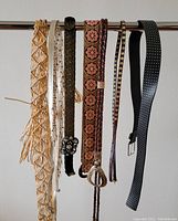 7 women's belts hanging from a rod showing various styles and materials, highlighting colors, buckles, and designs