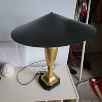 Full view of lamp showing wide painted brass conical shade, brass tapered body on black hexagonal base