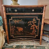 Front view showing black drawer and doors with gold Asian motif painting, bamboo frame