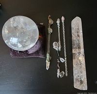 Photo of quartz crystal ball on black pillow, four crystal wands with some damage, and a large quartz crystal point. Items laid out on black surface.