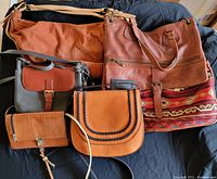 Group of five handbags and purses in various brown and orange tones arranged on dark fabric.