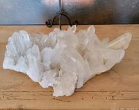 Large cluster of clear quartz crystals resting on a wooden surface showing multiple pointed crystal formations from a side angle.