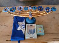 Menorah with blue flower candle holders, blue apron with Star of David, and two boxes of candles arranged on a wooden surface.