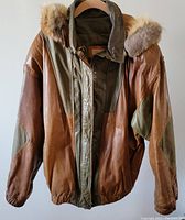 Front view of two-toned brown and olive leather men's hooded jacket with elastic cuffs and fur trim hood.