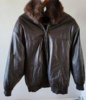 Front view of a women's dark brown leather bomber jacket with fur-lined hood, elastic cuffs, and waistband, front zipper, two angled pockets.