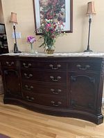 Front view of the dark carved wood sideboard buffet with floral arrangement and lamps on top, showing overall condition and surface wear.
