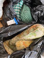 Three cushions and pillows visible inside black plastic bags including a floral tapestry cushion, a green striped pillow, and a blue and green plaid pillow.