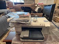 HP Photosmart D5360 printer with startup discs and black ink cartridge on top and nearby black monitor.