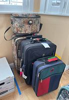 Overview of all four luggage pieces stacked near a window, showing floral overnight bag atop matching suitcase, with two smaller rolling suitcases nearby.