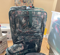 Front view of the two floral pattern suitcases stacked with overnight bag and toiletry bag in front, showing fabric pattern, straps, and zipper details
