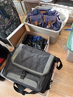 Photo showing Targus laptop bag front flap and carry handle, with various backpacks inside plastic storage bin and cardboard box