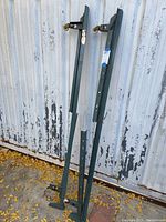 Two green metal adjustable bed frame side rails leaning against a wall, showing metal brackets and adjustment holes.