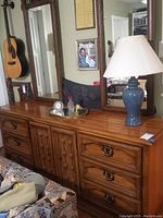 Full front view of vintage solid wood dresser showing two attached mirrors, drawers, and central cabinet doors with wood detailing. Items on top include a lamp and clock but are not included.