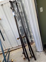 Metal parts of the vintage twin bed frame leaning against a wall. Side rails and legs are visible with dark finish and some wear.