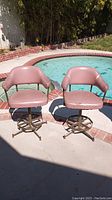 Front view of two vintage pink vinyl swivel chairs near swimming pool, showing wear and repair on upholstery.