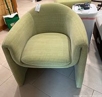 Front angled view of green fabric barrel chair showing shape, cushion and fabric texture.