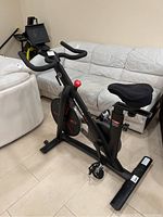 Side view of black Inspire IC1.5 stationary bike showing curved handlebars, electronics mount, and red adjustment knob.