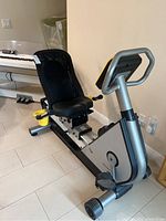 Side angle view of the LeMond Fitness G-Force RT recumbent exercise bike showing black mesh backrest, padded seat, aluminum handles and cup holders, pedals, and frame.