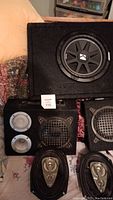 Kicker Stage 1 subwoofer in black carpeted enclosure with two small speaker boxes and two oval speakers in foreground.
