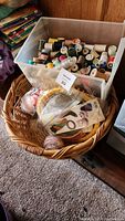 Plastic bin with assorted spools of threads, yarns, and floss along with a wicker basket containing crafting kits and tools.