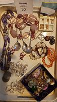 Full view of multiple beaded necklaces, silver-toned spoons, small jewelry box with earrings, and loose faux gem stones