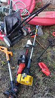 Photo of assorted gas and electric yard tools including lawn mower, weed eaters, hedge trimmers, and chainsaw cases on grass