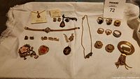 Overall photo showing the collection of gold-tone jewelry items spread on white cloth including rings, earrings, brooches, necklaces, and bracelet.