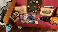 Overview of lot including wall clock, framed sketches, magazines, small desk fountain, bag of Mardi Gras coins, and other small items