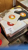 Multiple 45 RPM vinyl records with various labels and paper sleeves, stacked loose on a flat surface.