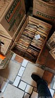 A packed U-Haul box filled with approximately 300 assorted 45 RPM vinyl record singles in paper sleeves, seen from above.
