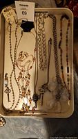 Photo showing various necklaces arranged in a tray including metal chains, key pendants, clear bead pendants, and multi-colored beaded necklace.