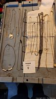 View of the multiple gold and silver toned necklaces laid on fabric and metal surface showing a variety of chain thicknesses and pendant designs