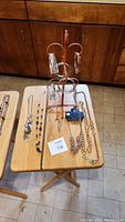 Wide view of multiple necklaces and bangle bracelets arranged on two folding wooden tables and a jewelry stand, showing styles and quantity.