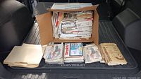 Box filled with a large quantity of miscellaneous sewing pattern envelopes, plus additional loose envelopes laid out in front of the box, showing various pattern designs and brands.