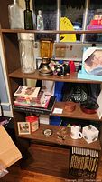 Wooden shelves holding various large books, glass bottles, lamp, decorative figurines, boxes, and bowls.