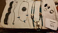 Full laid out view of all jewelry items including bracelets, necklaces, rings, and lapel pin on white cloth background