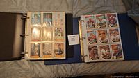 Two binders open on bed, showing pages of vintage sports cards including baseball and football cards.
