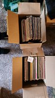 Two cardboard boxes filled with vintage vinyl records standing vertically showing a large quantity of albums.