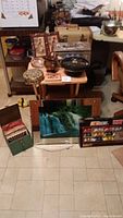 Wide view of assorted train luggage boxes, Japanese music box tins, glass ashtray, and foldable wooden trays on table. Copper pail and framed items visible in background.