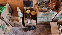 Photo capturing multiple boxes filled with assorted items including tins, toys, decorative pieces, and packaging materials.