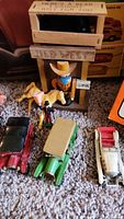 Photo of wooden cowboy figurine with horse and three vintage slot cars in red, green, and white colors on carpet surface.