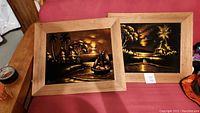 Two framed velvet art pieces showing Hawaiian tropical scenes including huts, palm trees, sailboats at sunset or dusk with warm brown and gold hues.