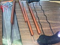 Two serrated meat tongs with wooden handles, metal skewers in blister pack, and Johnsonville branded metal food tents on wooden table.