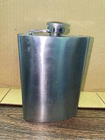 Front view of the stainless steel curved hip flask showing smooth surface and attached screw-top lid.