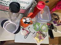 Overview of assorted kitchen items on table including bottles, storage containers, cookie cutters, utensils, and a ceramic holder.